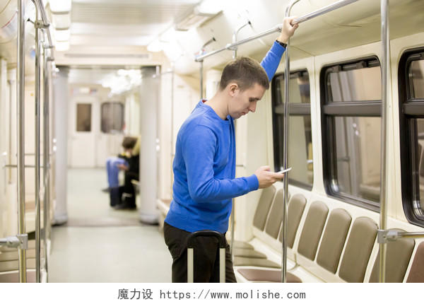年轻帅哥穿着休闲风格的服装站在地铁列车使用智能手机